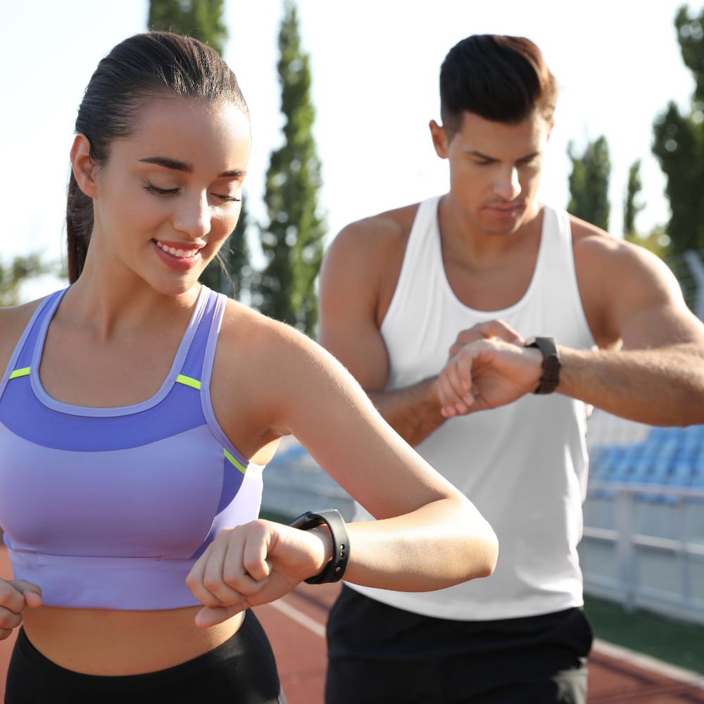 Woman in athletic wear checking her smartwatch with a man standing behind her outdoors.