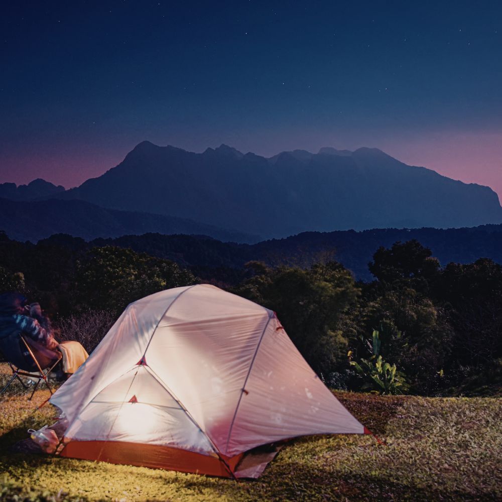 Camping tent illuminated at night with mountains in the background